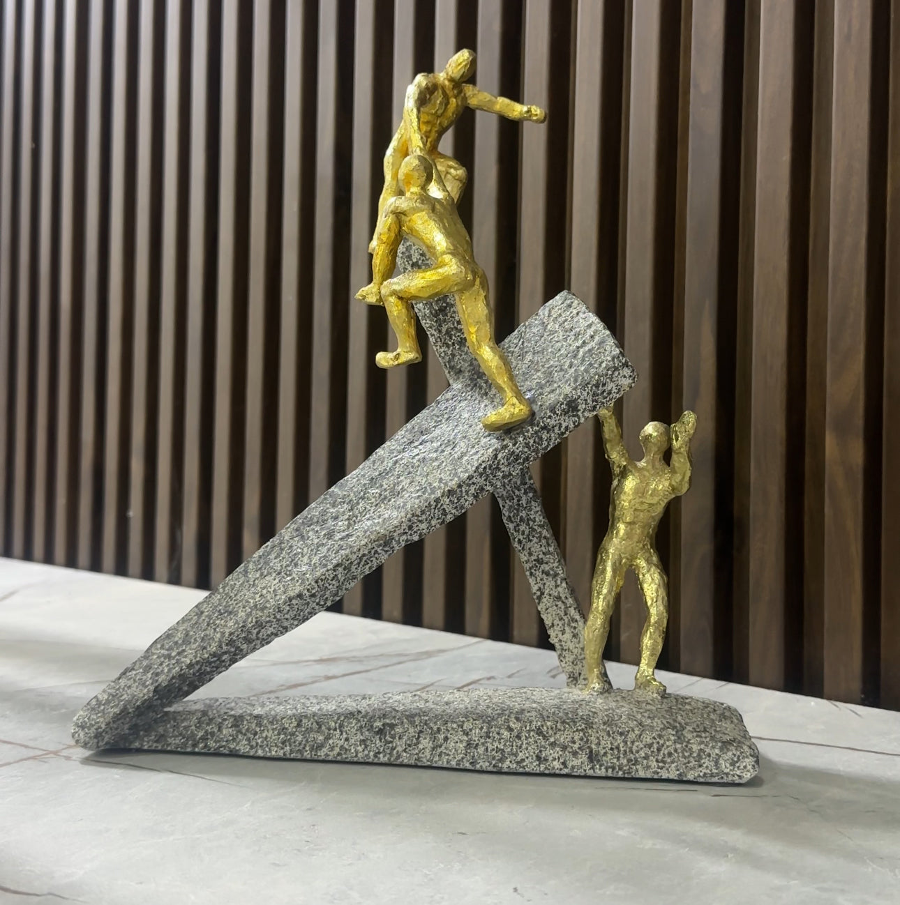 Statujë e 3 njerëzve ngjyrë gold duke u ngjitur në shkëmb