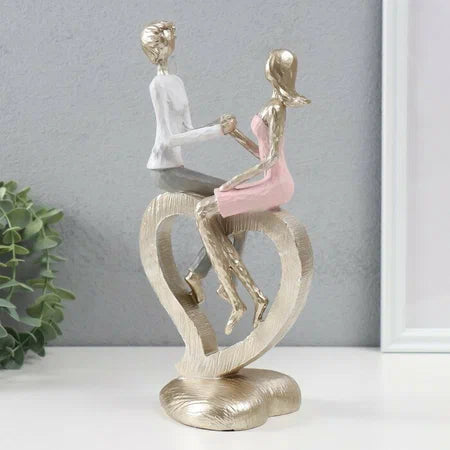 Statujë çift ulur mbi një zemër me duar të kapura, strukturë gold e ngjyrë rozë me të bardhë