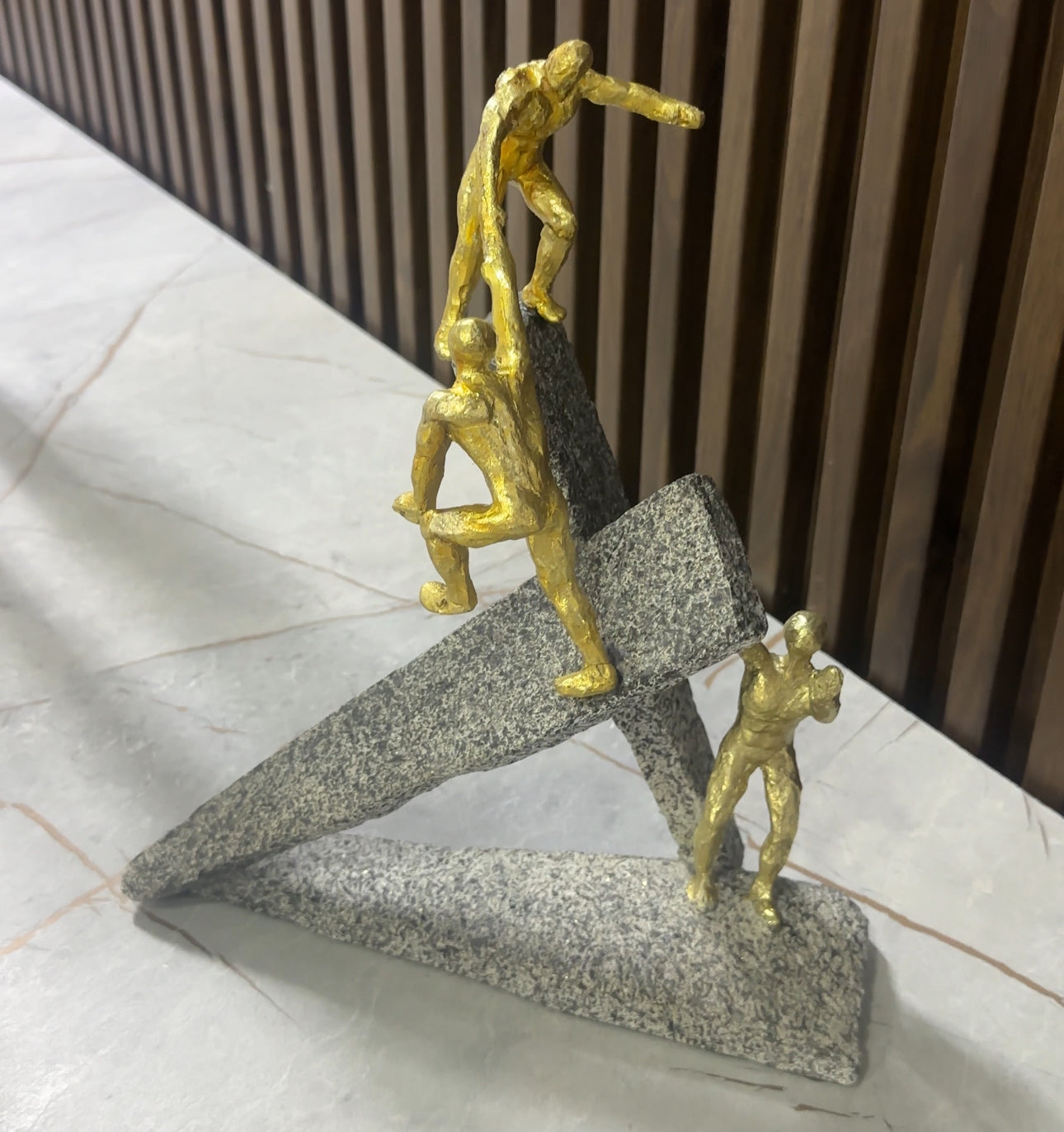 Statujë e 3 njerëzve ngjyrë gold duke u ngjitur në shkëmb