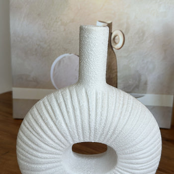 Vazo dekorative në formë rrethore me bisht të gjatë, me vijëzime vertikale dhe strukturë me kokrriza