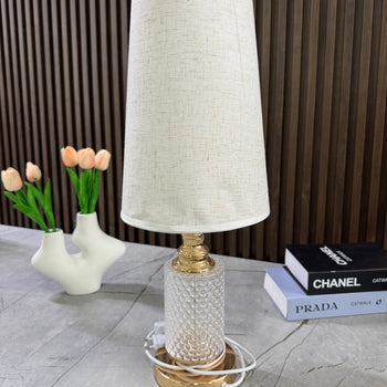 Llambë tavoline me bazë xhami të rrethuar metalike formë cilindrike dhe abazhur konik tekstili